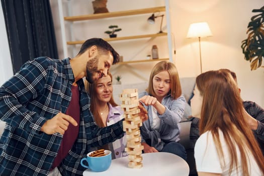 Wooden tower game on the table. Group of friends have party indoors together.