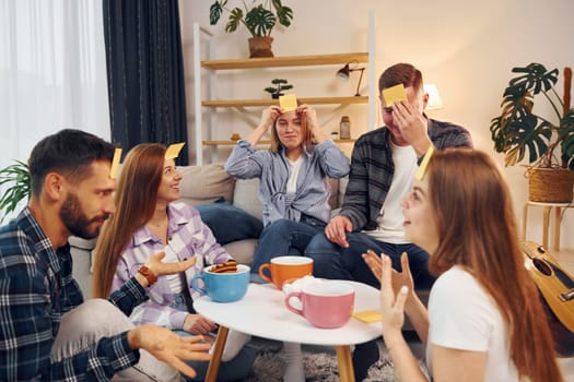 Yellow stickers on forehead. Group of friends have party indoors together.