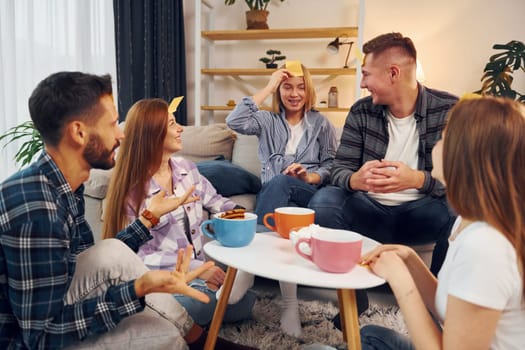 Yellow stickers on forehead. Group of friends have party indoors together.