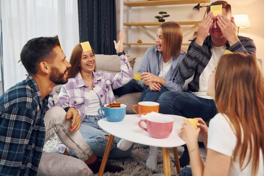 Yellow stickers on forehead. Group of friends have party indoors together.