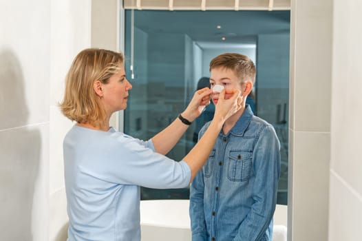 mom glues a patch to remove blackheads to her son. acne remover patch. teenage with nose band aid