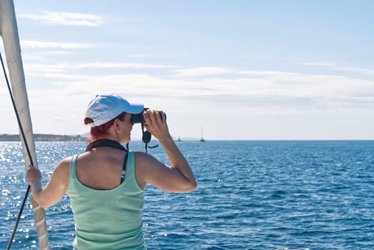 Girl on a yacht looking through binoculars. Happy female captain looks through a binoculars - marine concept