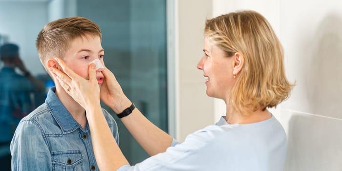 mom glues a patch to remove blackheads to her son. acne remover patch. teenage with nose band aid