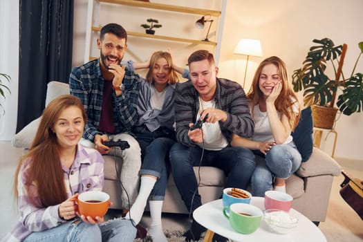 Playing video game. Group of friends have party indoors together.