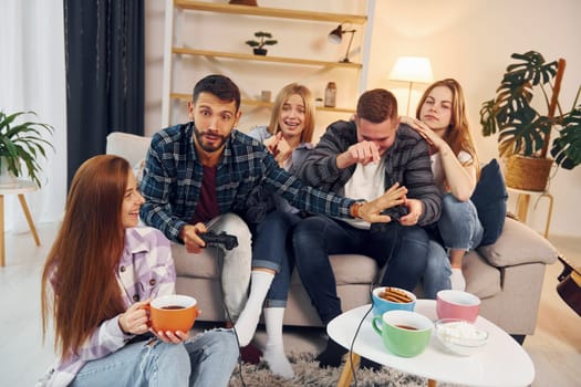 Playing video game. Group of friends have party indoors together.