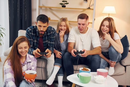 Using joysticks to play video game. Group of friends have party indoors together.