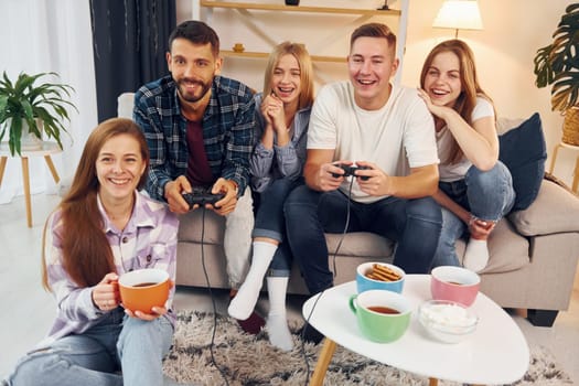 Using joysticks to play video game. Group of friends have party indoors together.