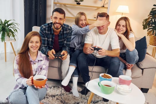 Using joysticks to play video game. Group of friends have party indoors together.