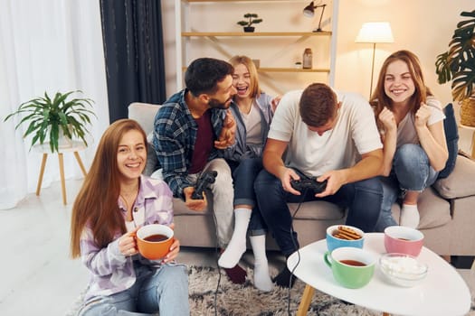 Using joysticks to play video game. Group of friends have party indoors together.