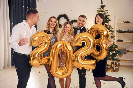 2023 balloons in hands. Group of people have a new year party indoors together.