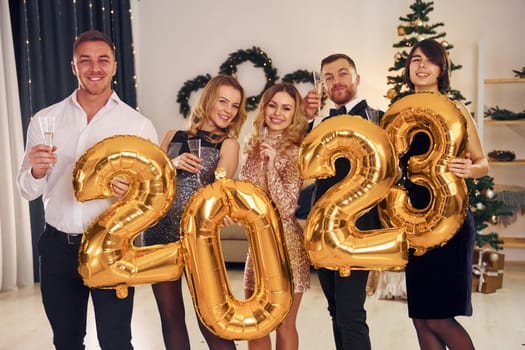 2023 balloons in hands. Group of people have a new year party indoors together.