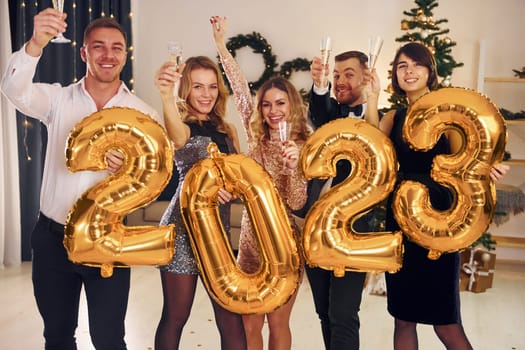2023 balloons in hands. Group of people have a new year party indoors together.