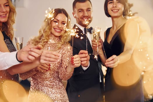 With sparklers in hands. Group of people have a new year party indoors together.