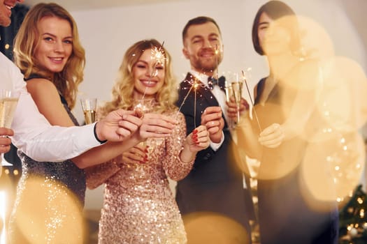 With sparklers in hands. Group of people have a new year party indoors together.