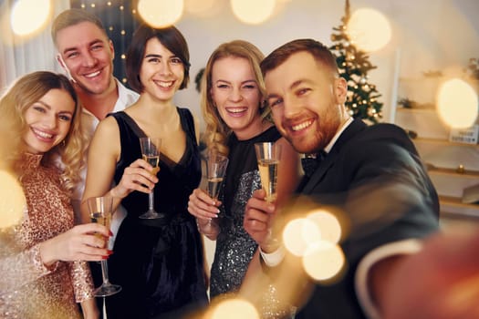 Holding phone. Group of people have a new year party indoors together.