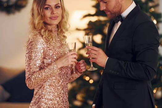 Standing against christmas tree. Happy couple have a new year party indoors together.