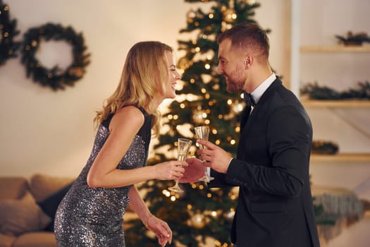 Cheering with glasses of alcohol. Happy couple have a new year party indoors together.