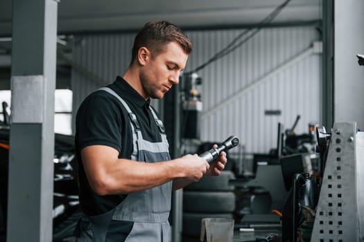 Holding tool. Man in uniform is working in the auto service.