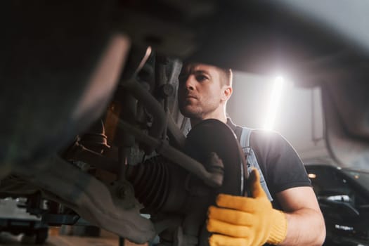 Fixing breaks. Man in uniform is working in the auto service.