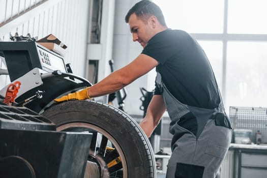 Taking the wheel. Man in uniform is working in the auto service.