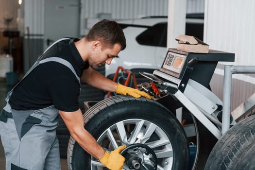 Taking the wheel. Man in uniform is working in the auto service.