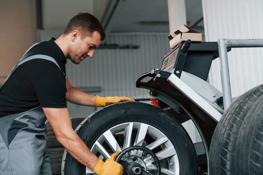 Taking the wheel. Man in uniform is working in the auto service.