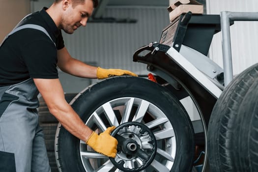 Fixing the tire. Man in uniform is working in the auto service.