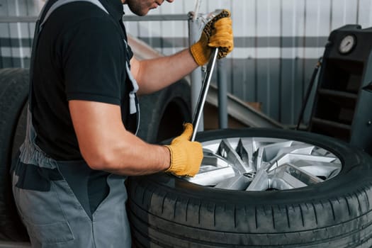 Working with broken wheel. Man in uniform is working in the auto service.