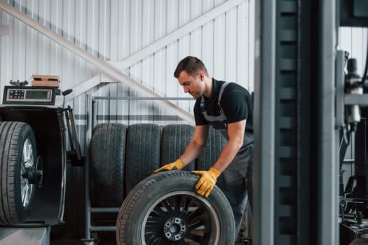 Working with broken wheel. Man in uniform is working in the auto service.