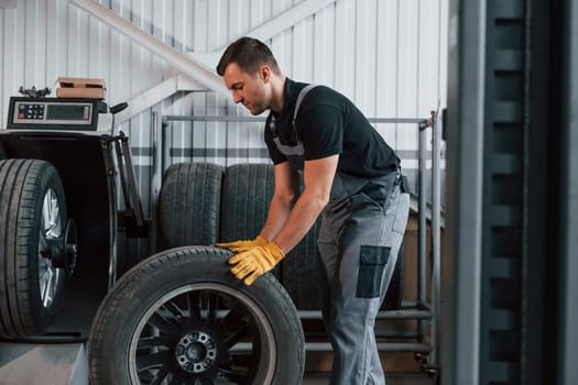 Working with broken wheel. Man in uniform is working in the auto service.