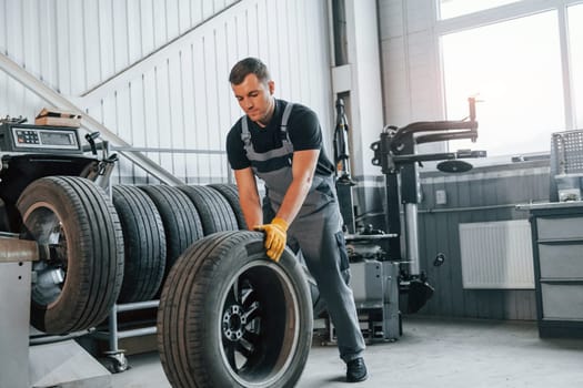 Working with broken wheel. Man in uniform is working in the auto service.