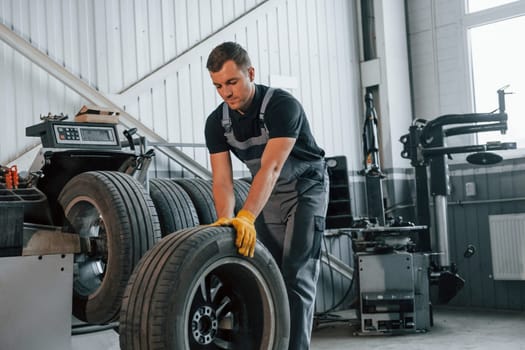 Walking with tyre. Man in uniform is working in the auto service.