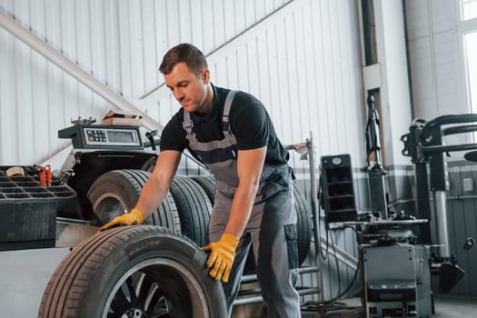 Walking with tyre. Man in uniform is working in the auto service.