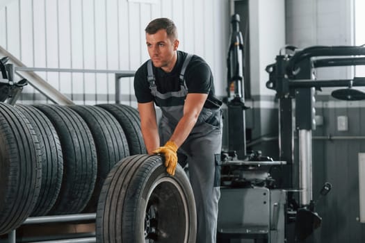 Walking with tyre. Man in uniform is working in the auto service.