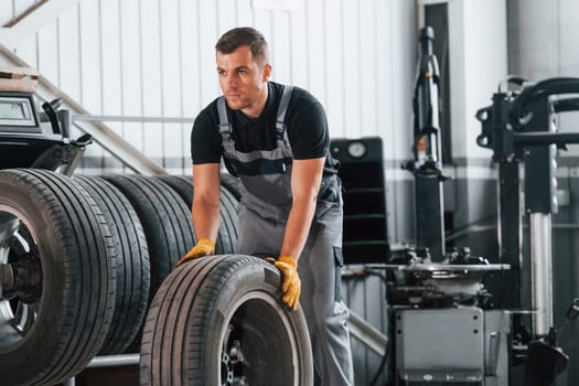 Walking with tyre. Man in uniform is working in the auto service.