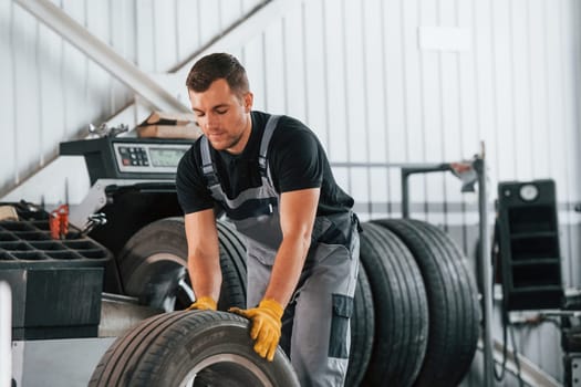 Replacement of the old tire. Man in uniform is working in the auto service.