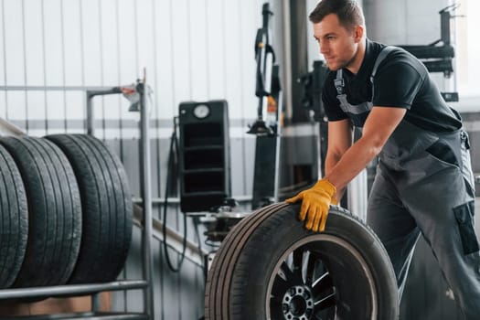 Replacement of the old tire. Man in uniform is working in the auto service.