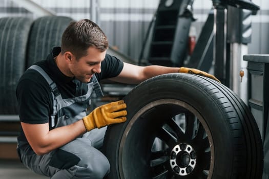 Replacement of the old tire. Man in uniform is working in the auto service.