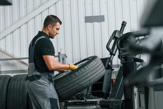 Walking and holding tyre. Man in uniform is working in the auto service.