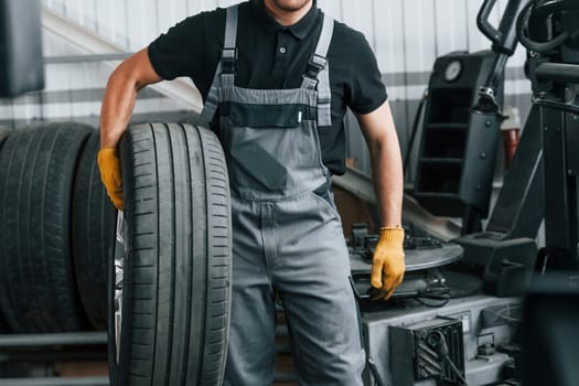 Walking and holding tyre. Man in uniform is working in the auto service.