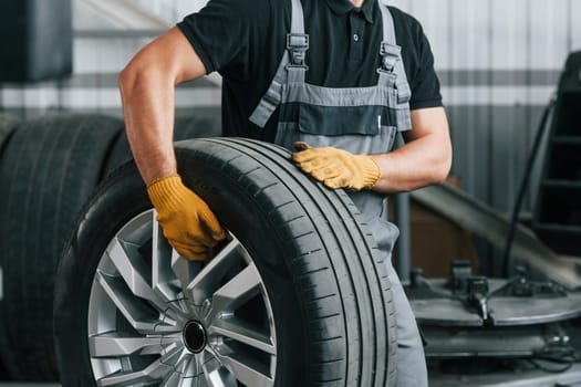 Walking and holding tyre. Man in uniform is working in the auto service.