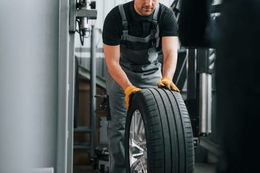 Close up view of wheel. Man in uniform is working in the auto service.