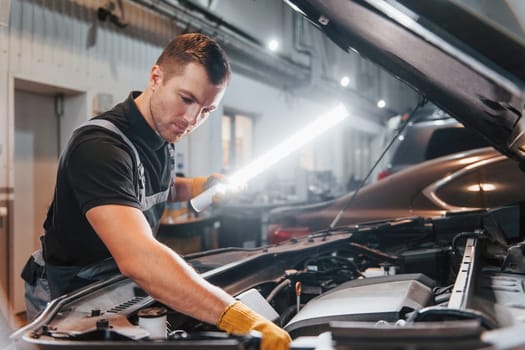 Under the hood. Man in uniform is working in the auto service.