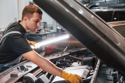 Under the hood. Man in uniform is working in the auto service.