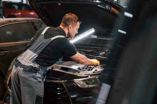 Under the hood. Man in uniform is working in the auto service.