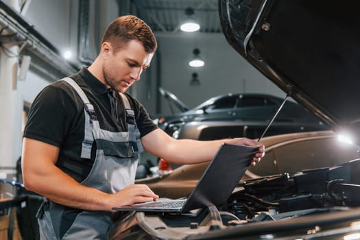 Side view. Man in uniform is working in the auto service.