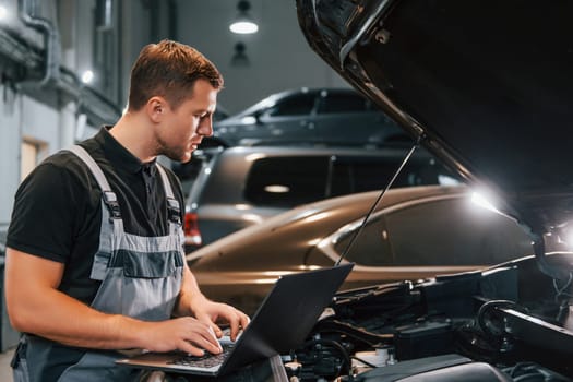 Side view. Man in uniform is working in the auto service.