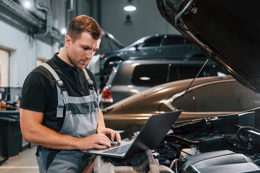 Using laptop. Man in uniform is working in the auto service.