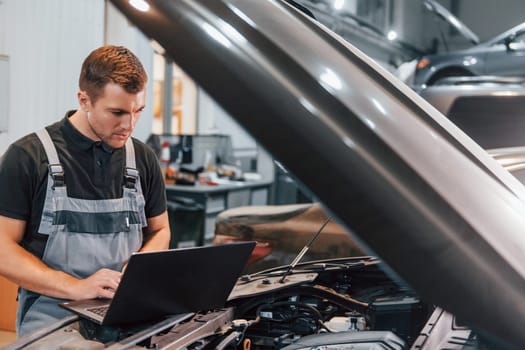 Using laptop. Man in uniform is working in the auto service.