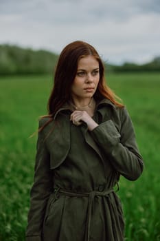 a beautiful woman stands in a green field and adjusts her coat. High quality photo